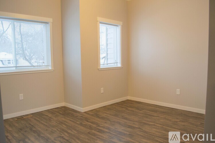 A room with wooden flooring and two windows.