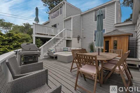 A wooden deck with a table and chairs is surrounded by a house and trees.