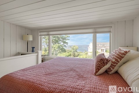 A bedroom with a red bedspread and a window overlooking the ocean.
