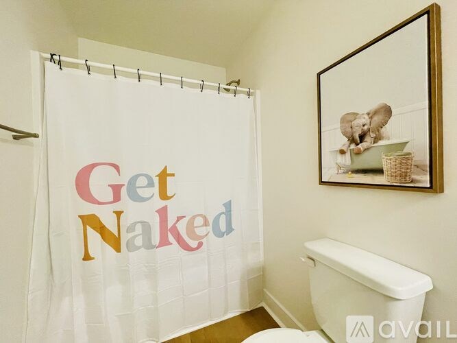 A bathroom with a shower curtain that says "Get Naked" and a picture of an elephant on the wall.