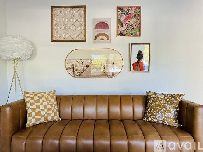 A brown leather couch with a yellow and gold pillow and a mirror on the wall.