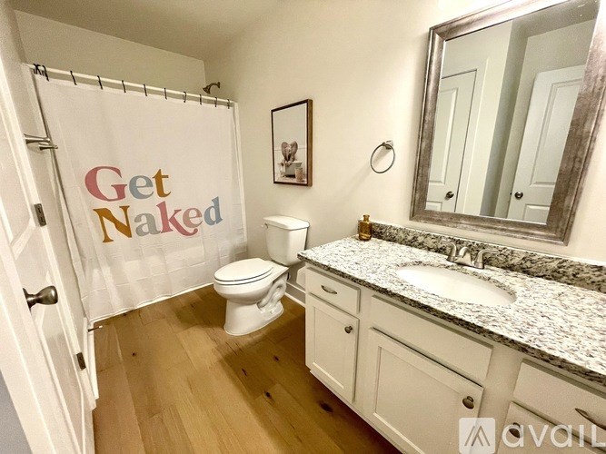 A bathroom with a toilet, sink, and a shower curtain that says "Get Naked".
