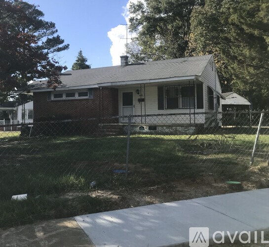 A small house with a white door and a chimney is surrounded by a fence.