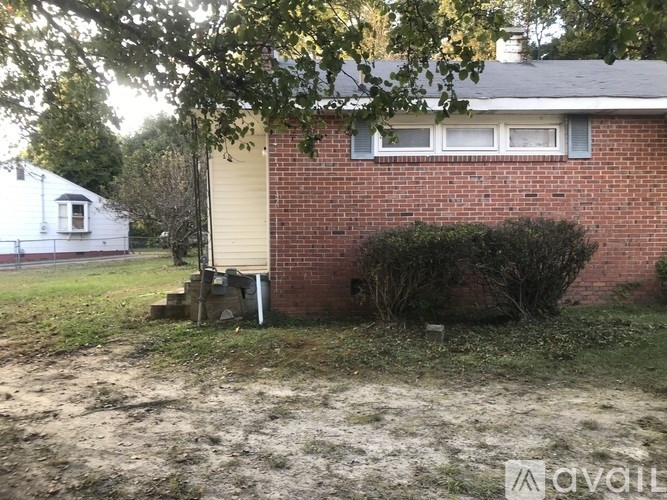 A red brick house with a white window and a small tree in front.