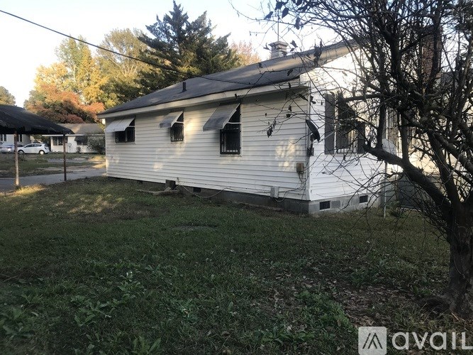 A small white house with a black roof and a tree in front.