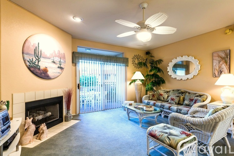 A living room with a fireplace, a couch, a chair, a coffee table, a potted plant, a mirror, and a painting on the wall.