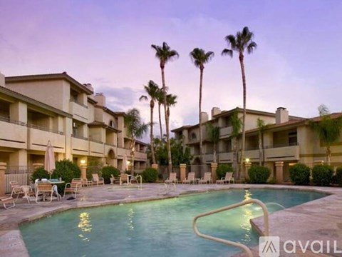 A swimming pool is surrounded by chairs and palm trees in front of apartment buildings.