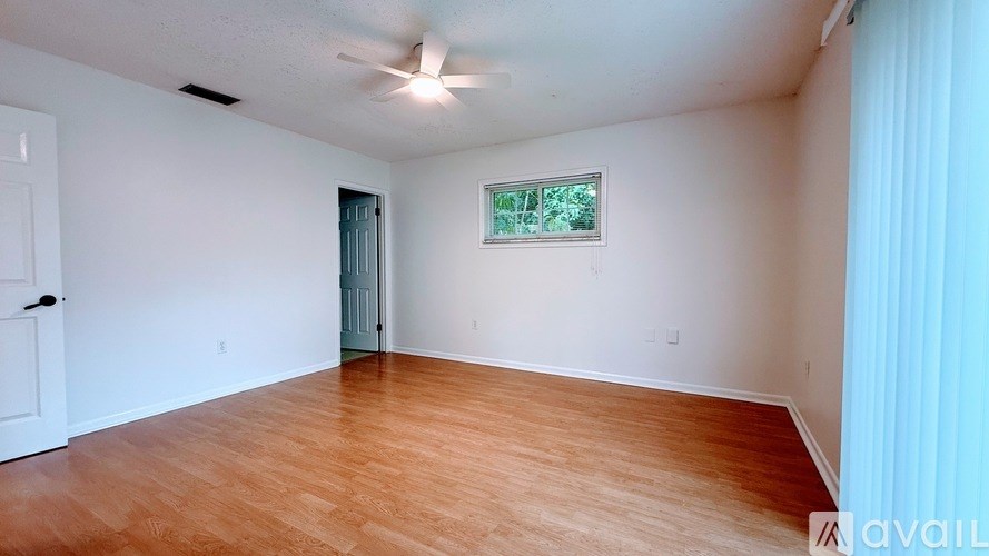 A room with wooden flooring and a window with a view of trees.