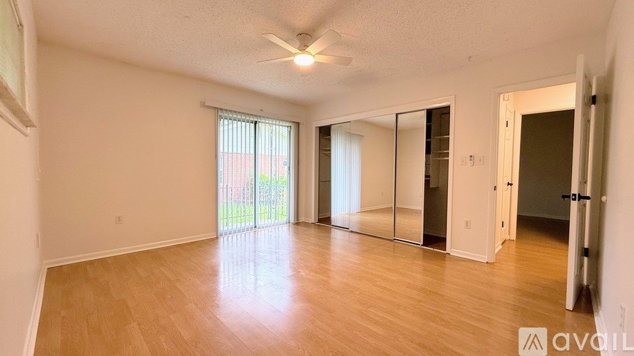 A spacious room with wooden flooring and a sliding glass door leading to a balcony.