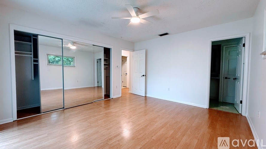 A room with wooden floors and white walls, with a glass door and a ceiling fan.