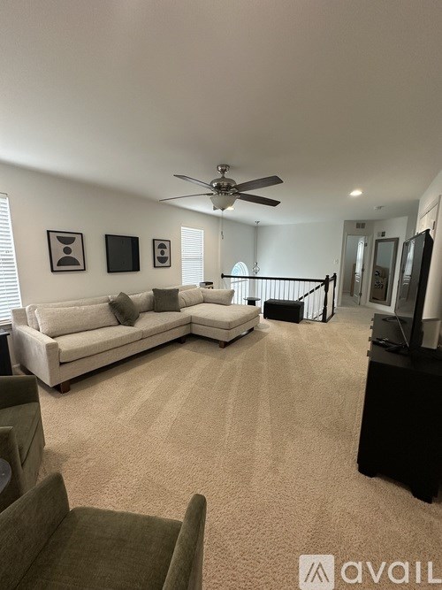 A living room with a white couch, a ceiling fan, and a staircase.