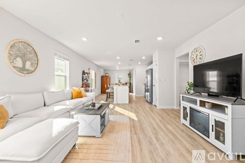 A living room with a white couch and a television on a white cabinet.