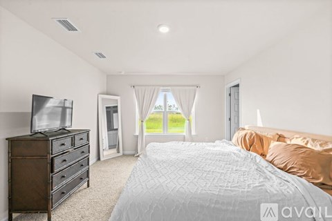 A bedroom with a large bed, a television, and a window with curtains.