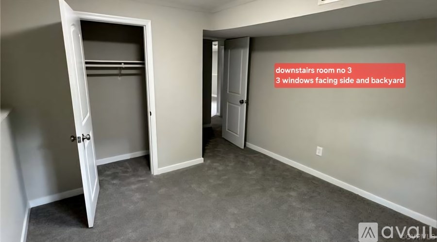 A room with a door open to a hallway and a wall with a sign that says "downstairs room no 3 3 windows facing side and backyard".