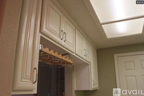 A kitchen with white cabinets and a shelf with clothes hanging on it.