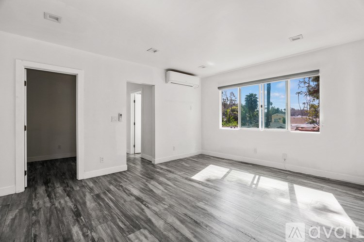 A room with a wooden floor and a large window showing a view of trees and a building outside.