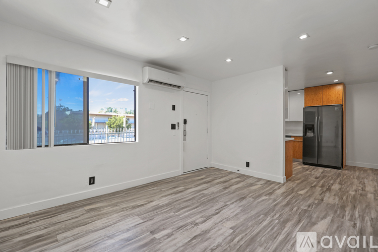 A spacious room with wood flooring and a large window with blinds.