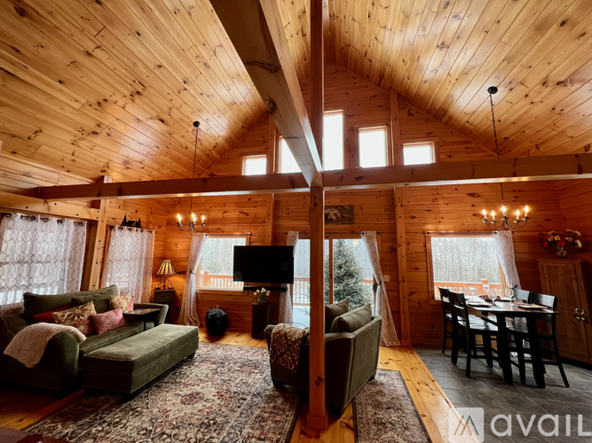 A cozy living room with wooden walls and ceiling, furnished with a sofa, armchair, and a dining table.