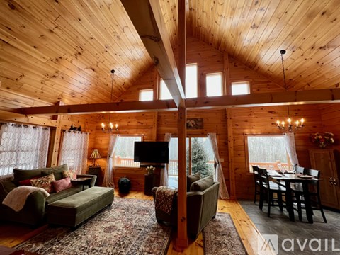 A cozy living room with wooden walls and ceiling, furnished with a sofa, armchair, and a dining table.