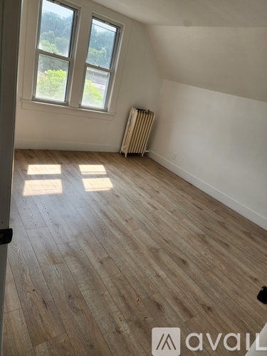 A room with wooden flooring and a window with a view of trees.