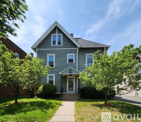 A two-story house with a front porch and a tree in front.