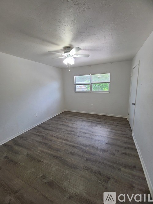 A room with wooden flooring and a window showing greenery outside.