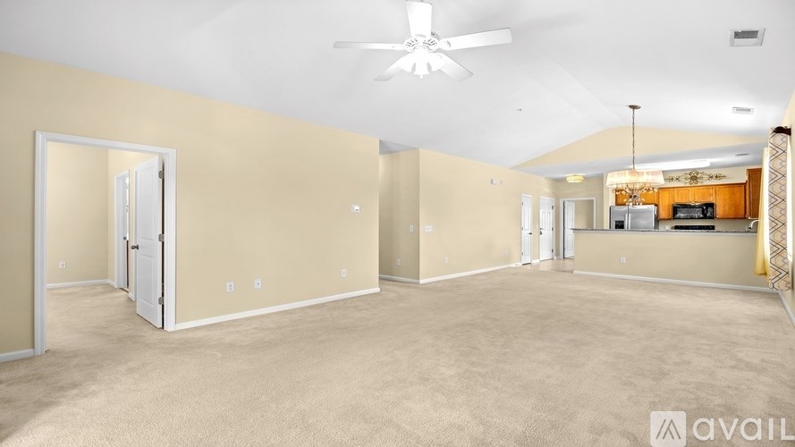 A spacious room with beige walls and carpeting, featuring a ceiling fan and a door with a mirror.
