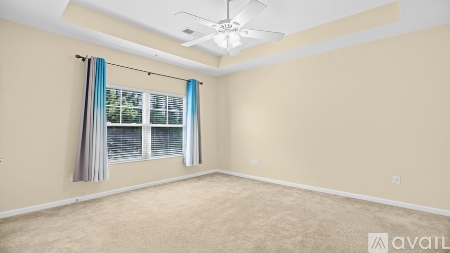 A room with beige walls, a ceiling fan, and a window with blue curtains.