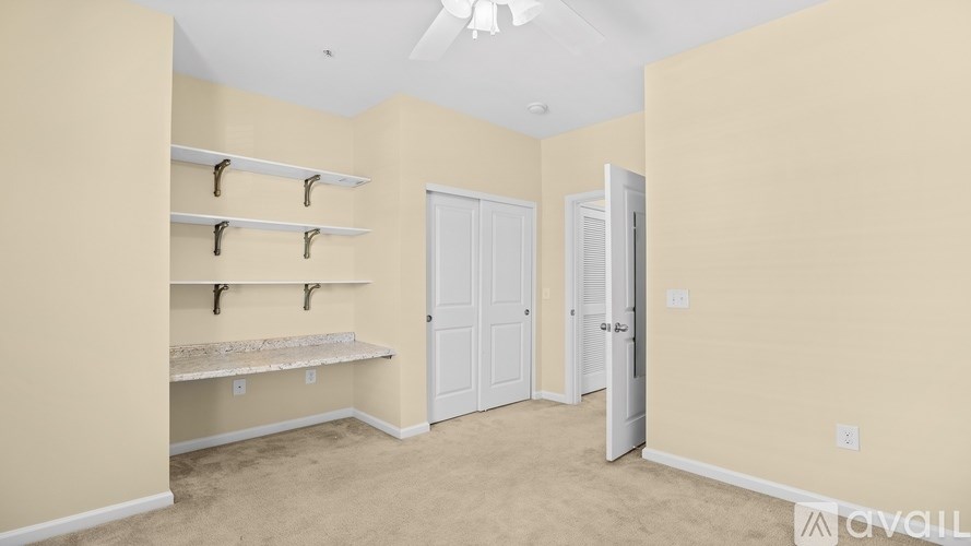 A room with a carpeted floor, a ceiling fan, and a doorway leading to another room.