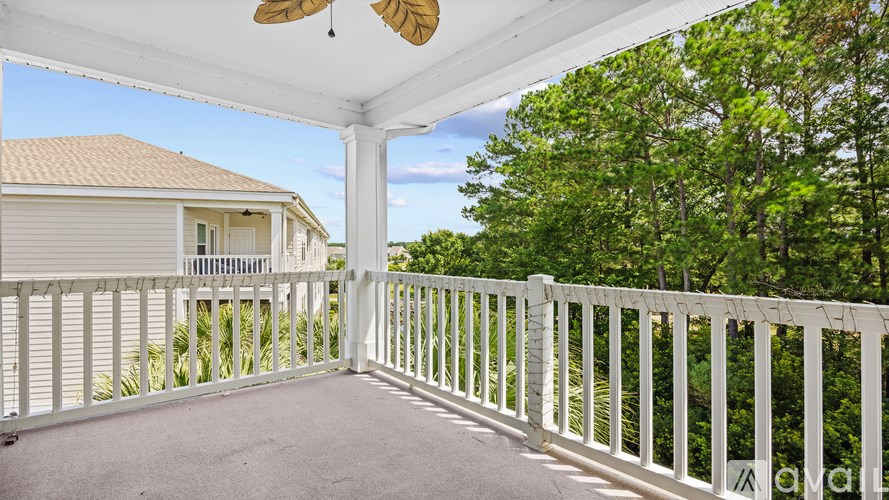 A white porch with a fan and trees in the background.