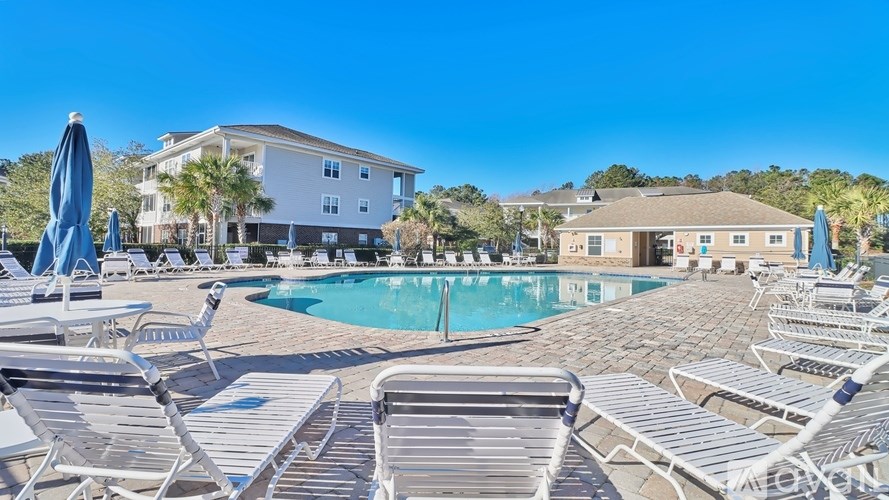 A pool area with sun loungers and umbrellas in front of a building.
