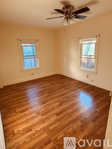 A room with wooden flooring and two windows.