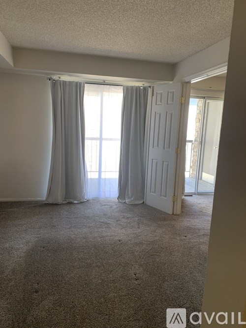 A room with a carpeted floor and a large window with curtains.