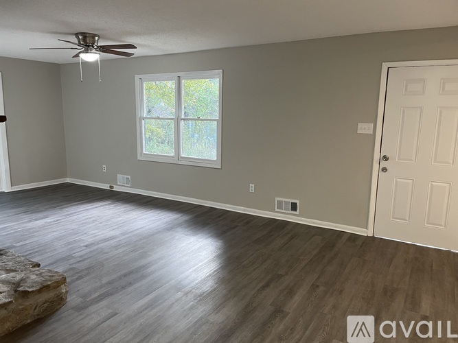 A room with a ceiling fan and a window with a view of trees.