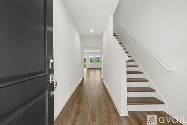 A hallway with a staircase on the right and a black door on the left.