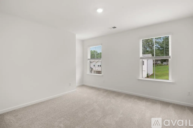 A spacious room with a carpeted floor and two windows, one of which shows an outdoor view.