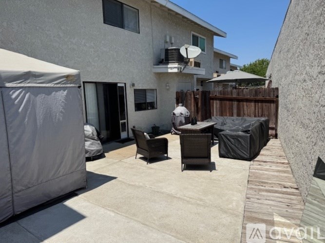 A patio with a white umbrella and a black grill.
