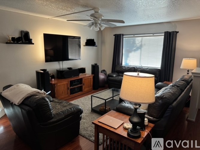 A living room with a black leather couch, a television, and a ceiling fan.