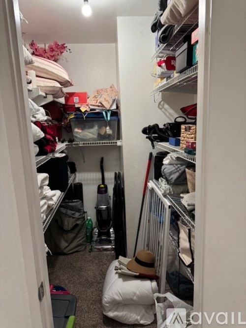 A small closet with a lot of clothes and a hat on the floor.