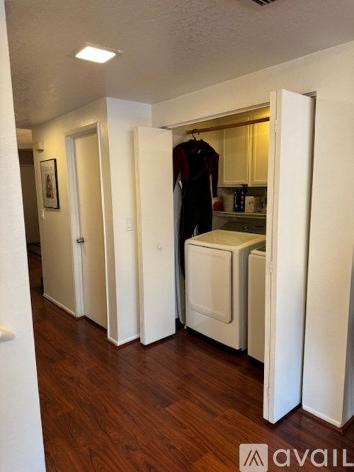 A hallway with a coat hanging on the door and a washer and dryer stacked in the kitchen.