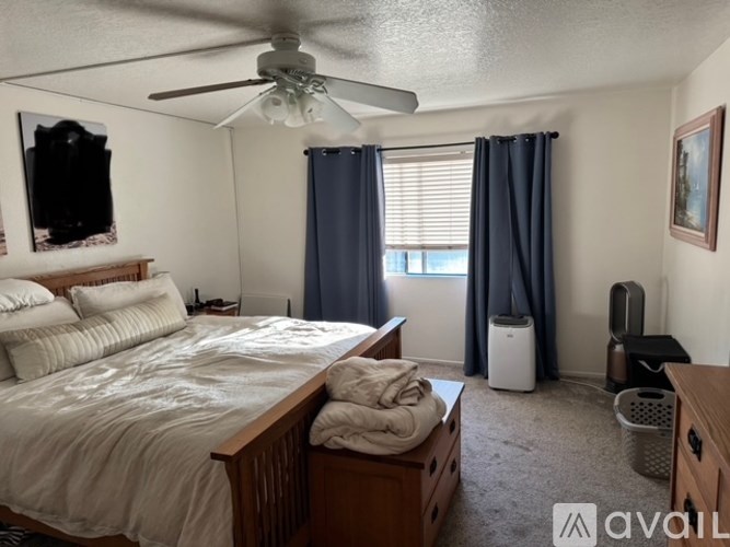 A bedroom with a bed, a fan, and a window with curtains.