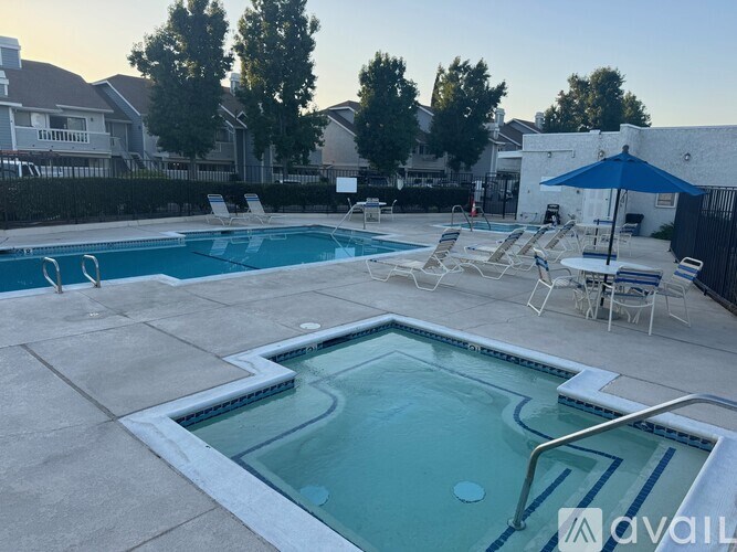 A pool with a hot tub and chairs is surrounded by a fence and houses.