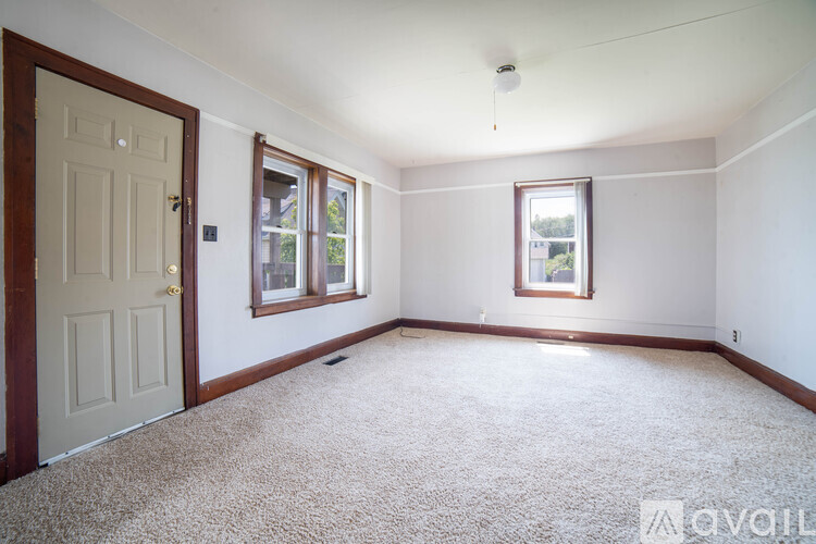 A room with a carpeted floor, a door, a window with a view of trees, and a picture on the wall.