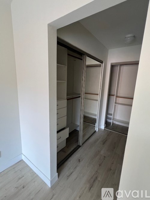 A hallway with a white wall and a wooden floor leading to a closet.