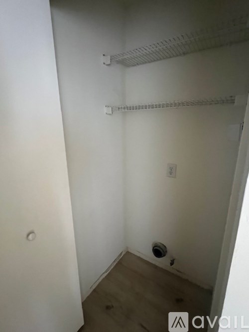 A small, empty room with a white wall and a wooden floor.