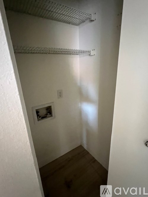 A small white room with a picture on the wall and a shelf above it.