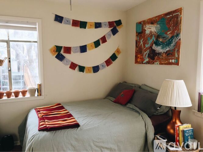 A bedroom with a bed, a lamp, and a colorful wall hanging.