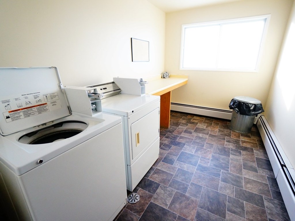 A white washing machine is in a room with a tiled floor and a window.