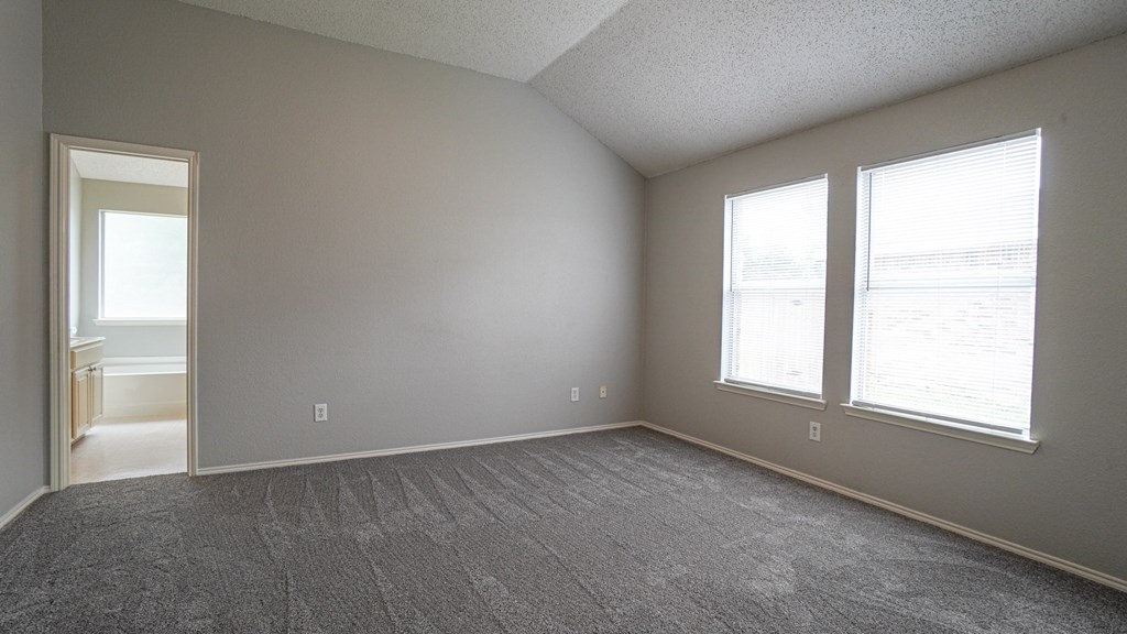 A room with a carpeted floor and two windows.