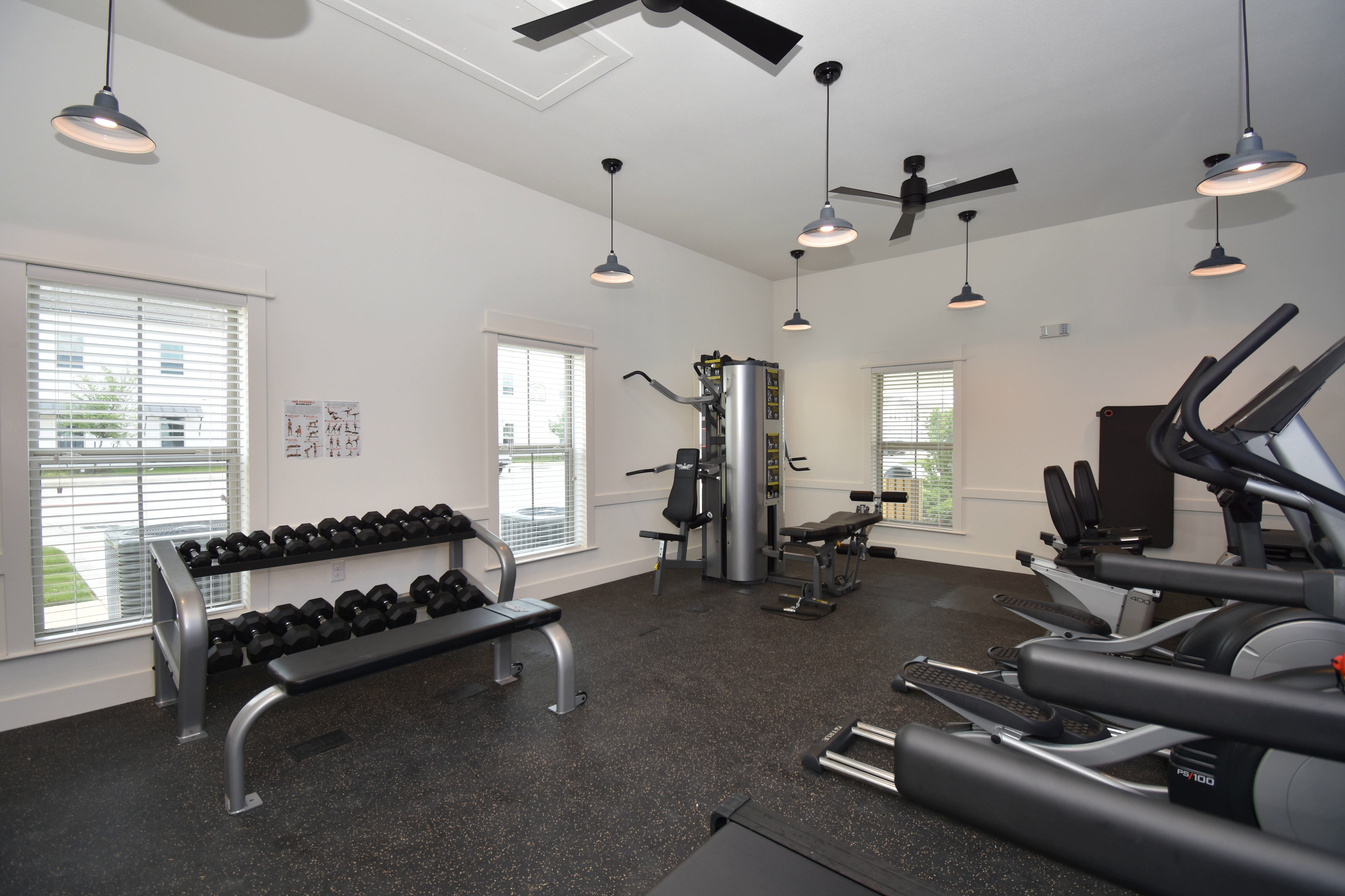 A gym with a row of treadmills and a bench with dumbbells.